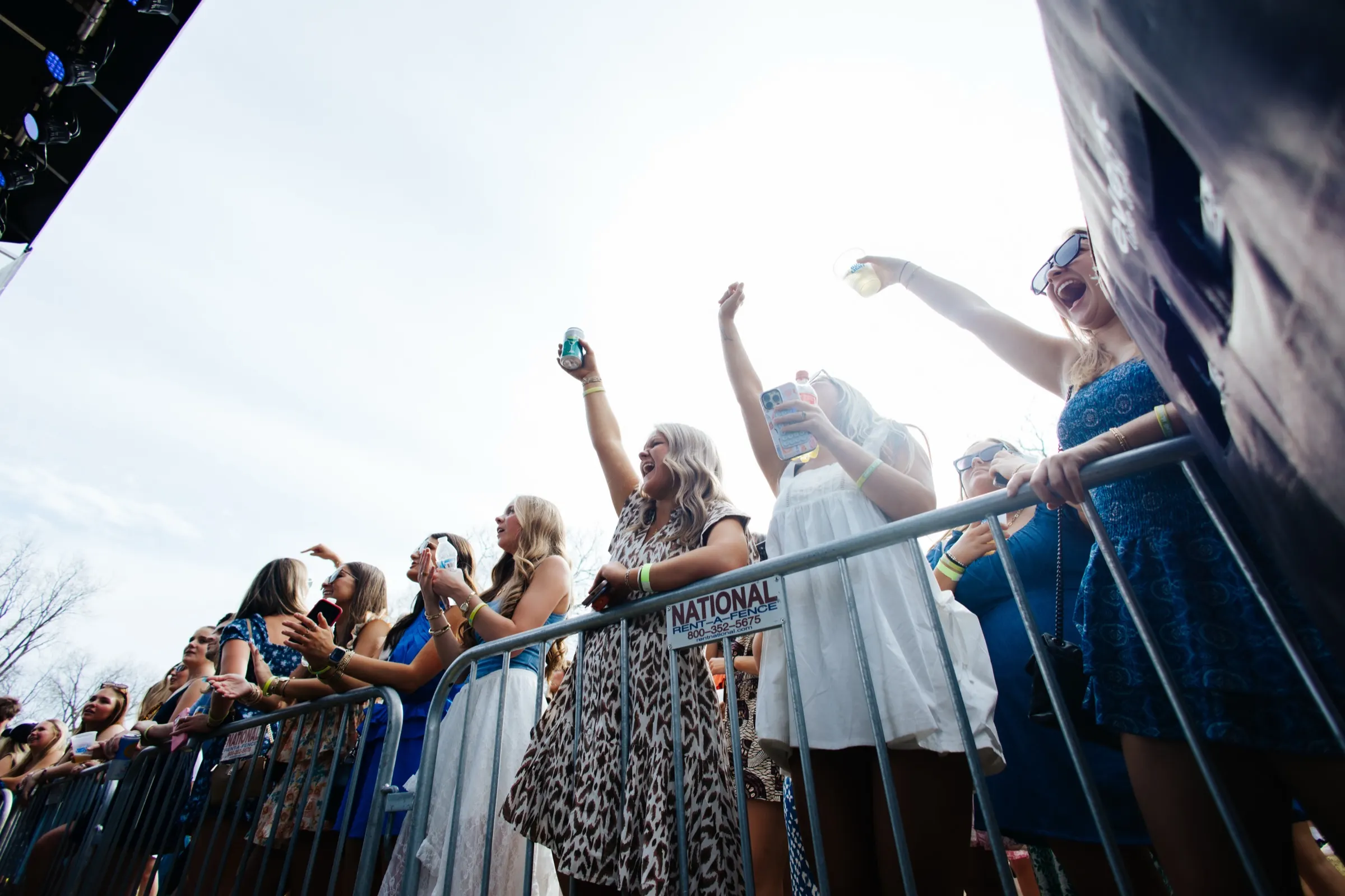 Fans cheering at the front barricade under a bright sky