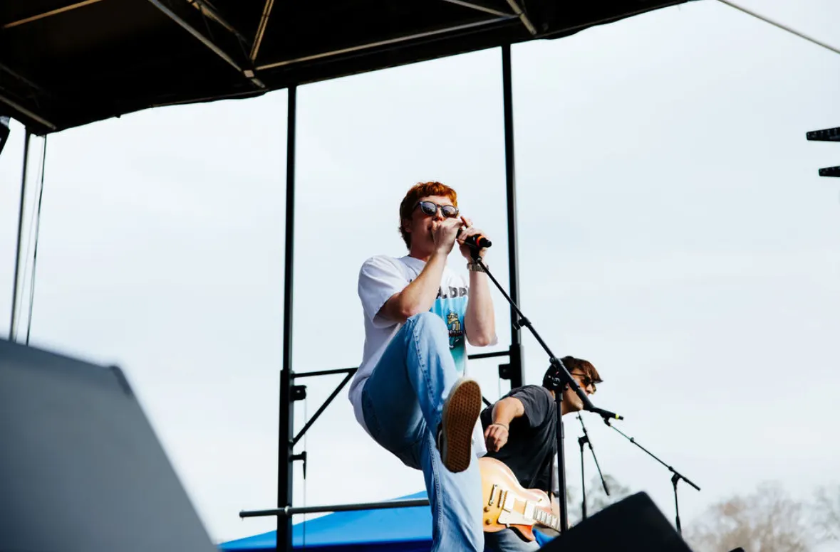 A singer leans into the mic against the open sky