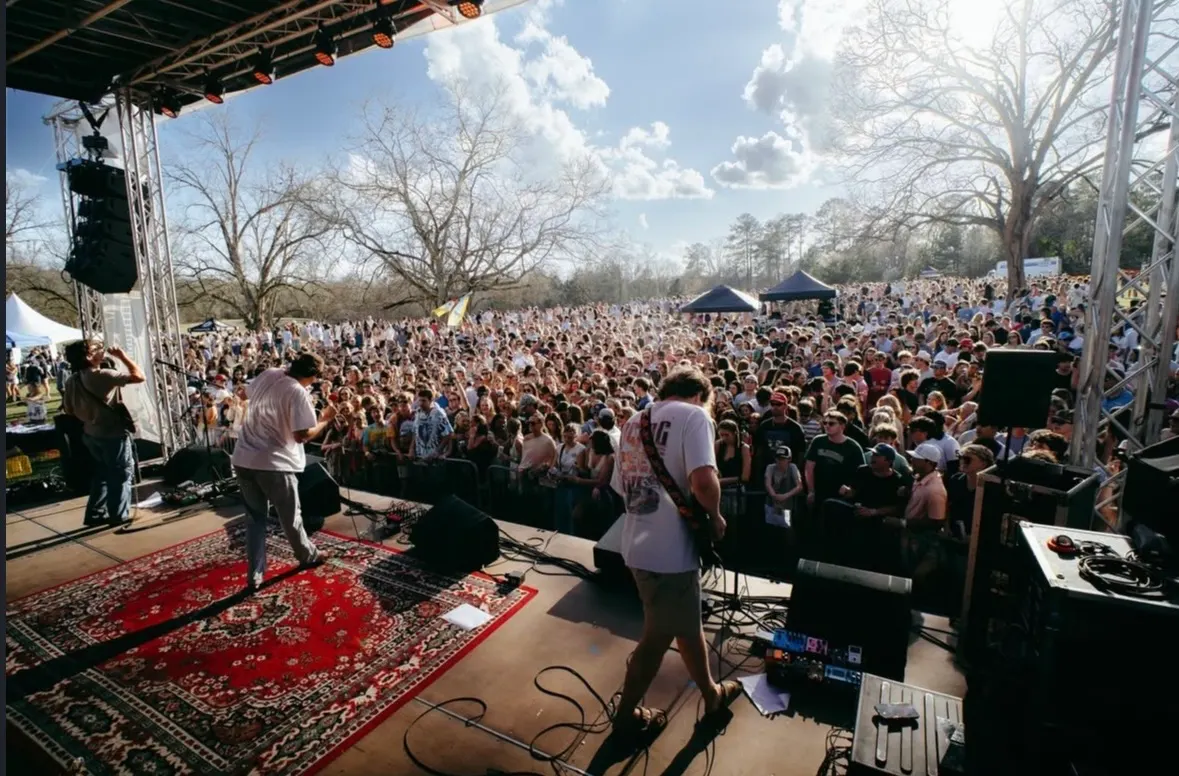 A band on a rug-covered stage looking out at a packed field