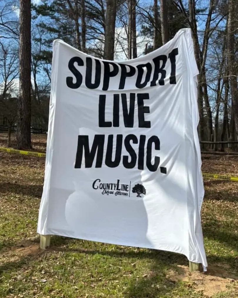 A Support Live Music banner hanging among the pines
